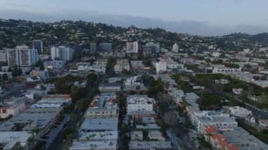 Gün batımından sonra şehir merkezindeki binaların üzerinden uç. Şehrin üstündeki tepeler gökyüzüne karşı. Los Angeles, Kaliforniya, ABD