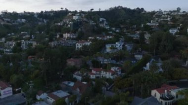 Yokuşta inşa edilmiş lüks konutların üzerinde uç. Alacakaranlıkta yeşil bitki örtüsüyle çevrili mülkler. Los Angeles, Kaliforniya, ABD