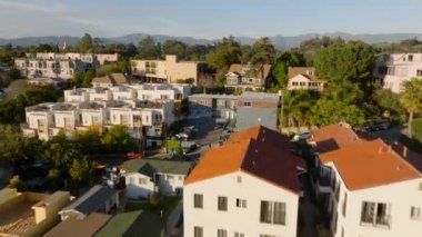 Parlak güneş ışığıyla aydınlatılmış konutların üzerinde alçak uçuş. Kamu parkındaki yeşil bitki örtüsünü gözler önüne seriyor. Los Angeles, Kaliforniya, ABD.