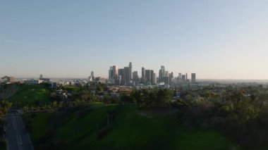 Şehirdeki yeşil bitki örtüsünün havadan panoramik görüntüsü ve temiz gökyüzüne karşı şehir merkezindeki ünlü gökdelenlerle gökyüzü. Los Angeles, Kaliforniya, ABD.