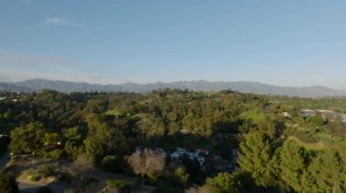 Şehrin eteklerindeki yeşil bitki örtüsüyle çevrili konutların üzerinde uçuyorlar. Los Angeles, Kaliforniya, ABD.