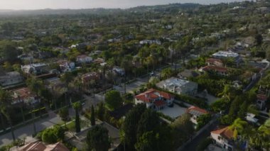 Beverly Hills 'in altın saatindeki hava kaydırağı ve pan görüntüleri. Palmiye ağaçları ve lüks konutlarla dolu bir cadde. Los Angeles, Kaliforniya, ABD