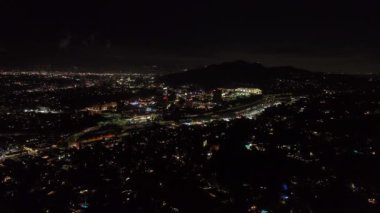 İleri, gece şehrinin üzerinde uçar. Universal City 'deki aydınlık binaların etrafında çok şeritli otobanda giden arabalar. Los Angeles, Kaliforniya, ABD.