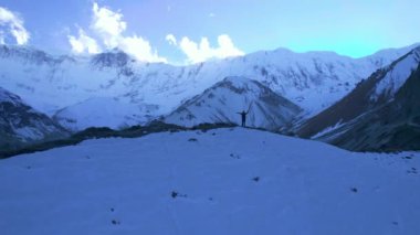 Yuvarlak hava manzaralı erkek yürüyüşçü tepenin üstünde kollarını havaya kaldırarak yürüyüş hedefine ve amacına ulaşmanın tadını çıkarıyor. Açık havada seyahat, Himalaya, Asya, Tilicho 'da yürüyüş..