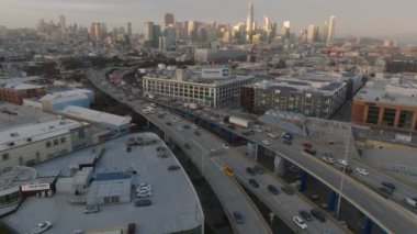 Metropolis 'teki yoğun çoklu şeritli otobanda yavaşça hareket eden araçların üzerinden uç. Şehir merkezindeki gökdelenler gün batımını yansıtıyor. San Francisco, California, ABD