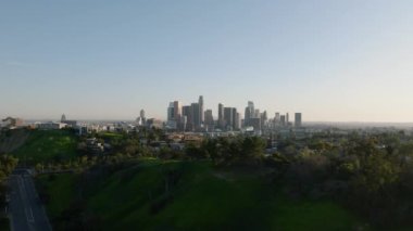 Şehirdeki yeşil bitki örtüsünün havadan panoramik görüntüsü ve temiz gökyüzüne karşı şehir merkezindeki ünlü gökdelenlerle gökyüzü. Los Angeles, Kaliforniya, ABD.