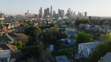 Şehir merkezindeki evlerin üzerinden uçuyor. Finansal bölgedeki bir grup gökdelen arka planda. Los Angeles, Kaliforniya, ABD.
