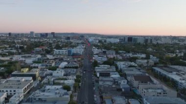 Günbatımında geniş caddenin ve kentsel çevredeki binaların üzerinde ilerliyorlar. Los Angeles, Kaliforniya, ABD