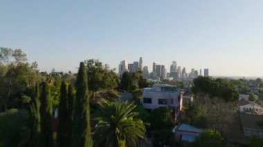 Konutlarla tepenin üzerinden uçun. Finansal bölgedeki şehir manzaralarını ve gökdelenleri gösteriyor. Los Angeles, Kaliforniya, ABD.