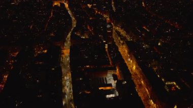 Aydınlatılmış iki cadde arasındaki binaların üzerinde uç. Geceleri şehir merkezinin havadan görünüşü. Barselona, İspanya.