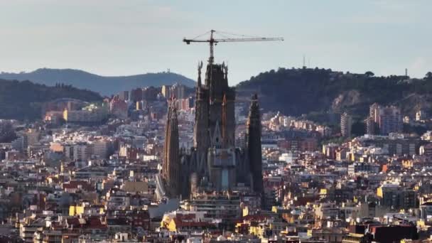 サグラダ ファミリアの建設でクレーンのズームショット 周囲の町の開発の上にそびえる有名な大聖堂 スペインのバルセロナ — ストック動画