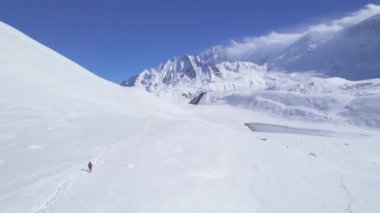 Solo erkek yürüyüşçülerin karlı patikada sırıklarla yürürken çekilen hava yavaş uçuşu. Nepal popüler yürüyüşleri. Manang bölgesi Annapurna yürüyüş pisti