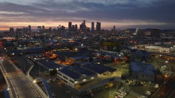 夜の街の空撮 夕暮れ時の照明付きの通りや建物 カラフルな空に対する超高層ビルのシルエット 米国カリフォルニア州ロサンゼルス — ストック動画