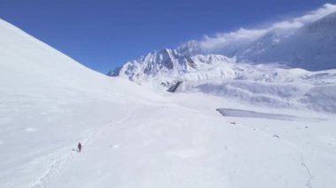 Solo erkek yürüyüşçülerin karlı patikada sırıklarla yürürken çekilen hava yavaş uçuşu. Nepal popüler yürüyüşleri. Manang bölgesi Annapurna yürüyüş pisti