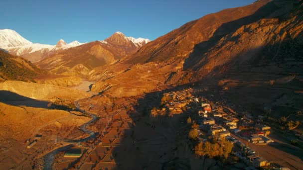 高い山の景観で雄大な谷の上を飛ぶ ゴールデンタイムの川と典型的な村 マナンバレー アンナプルサーキットトレック ネパール — ストック動画