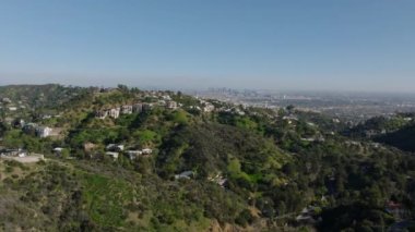 Metropolis 'in yukarısındaki tepelerdeki yerleşim yerlerinin üzerinde ilerliyorlar. Şehir merkezindeki gökdelenlerden oluşan bir grup. Los Angeles, Kaliforniya, ABD.