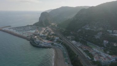 Deniz ve dik tepeler arasında şehrin hava panoramik görüntüleri. Demiryolu rayları ve etrafından geçen yollar. Garraf, İspanya.