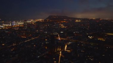 Gece metropolün üzerinde ilerliyorlar. Tarihi semtteki binalar ve uzak mesafeden aydınlık limanlar. Barselona, İspanya.