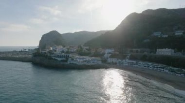 Küçük bir kasaba ve marinayla deniz kıyısının kaygan görüntüsü, arka planda sarp kayalıklar. Alçak güneşe karşı görüş. Garraf, İspanya.