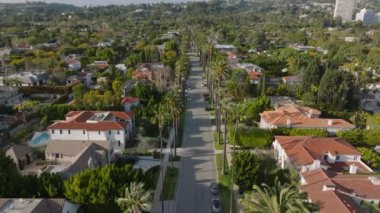 Lüks bir yerleşim bölgesinde sakin bir caddenin üzerinde ilerliyorlar. Beverly Hills 'teki yeşilliklerle çevrili konutların havadan görüntüsü. Los Angeles, Kaliforniya, ABD