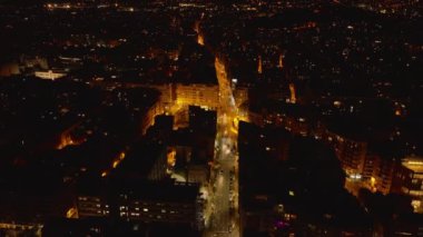 Caddelerde giden ve kavşağı geçen arabaların hava görüntüleri. Gece şehrindeki sarı sokak lambaları. Barselona, İspanya.