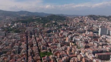 İleri, şehrin üzerinde uçar. Şehir merkezlerindeki binalar ve arka plandaki ağaçlık tepeler. Barselona, İspanya.