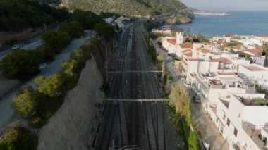 İleri, küçük sahil kasabasından geçen çok raylı demiryolu hattının üzerinden uçar. Gölgeler ve doğrudan güneş ışığı. Garraf, İspanya.