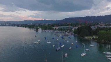 Göl kıyısı ve Aquaretum çeşmesi yakınlarındaki yelkenli teknelerin üzerinden ileri doğru uçar. Alacakaranlıkta sakin su yüzeyi. Zürih, İsviçre.