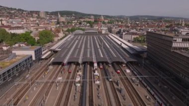 İleri, ana tren istasyonunun üzerinden uçun. Çatı peronu ve raylardaki yolcu trenleri. Şehirdeki demiryolu altyapısının havadan görüntüsü. Zürih, İsviçre.