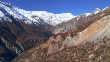 Himalaya dağları güneşli bir günde manzaraya sahiptir. Kayalık yamaçlarla çevrili derin vadi ve karla kaplı tepeler. Manang Vadisi, Annapurna Gezisi, Nepal.