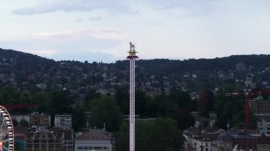 Lunaparktaki uzun kulenin kaydırak ve arka plan görüntüleri. Renkli neon ışıklar yanıp sönüyor ve etrafındaki binaların camlarına yansıyor. Zürih, İsviçre.