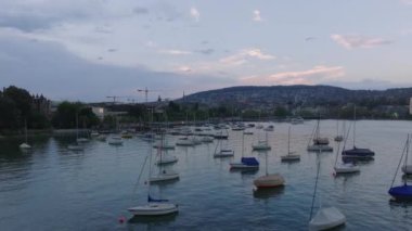 Yat limanına demirlemiş yelkenli teknelerinin etrafından dolaş. Alacakaranlıkta şehirde sakin bir göl yüzeyi. Zürih, İsviçre.