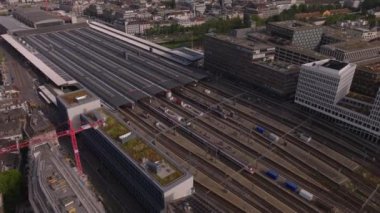 Şehrin gelişimine yüksek açılı bir bakış açısı. İstasyondan ayrılan banliyö trenleriyle Hauptbahnhof 'un üzerinden uç. Yukarı kaldır ve arka planda şehir manzarası ve gölü göster. Zürih, İsviçre.