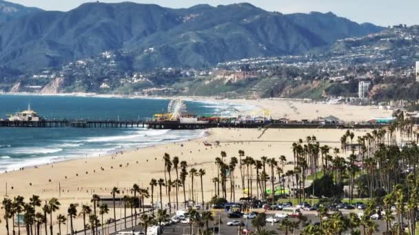 サンタモニカ桟橋と背景の山々に太平洋公園の拡大した空中静的ショット 海岸沿いの砂浜 米国カリフォルニア州ロサンゼルス — ストック動画