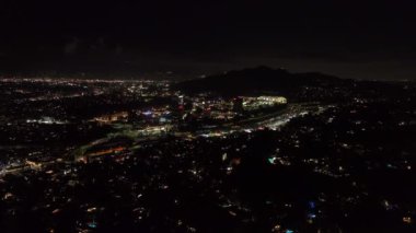 İleri, gece şehrinin üzerinde uçar. Universal City 'deki aydınlık binaların etrafında çok şeritli otobanda giden arabalar. Los Angeles, Kaliforniya, ABD.