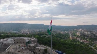 Tuna nehri üzerindeki Gellert Tepesi 'ndeki tarihi kalede milli bayrak etrafında yörünge atışı. Macar bayrağı ve şehir manzarası. Budapeşte, Macaristan.