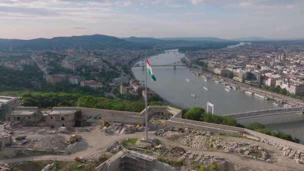 ゲラートヒルの頂上にある歴史的な要塞の上を飛行してください ハンガリーの国旗がシタデラの街の広い川のドナウ川の上を飛んでいる ブダペスト ハンガリー — ストック動画
