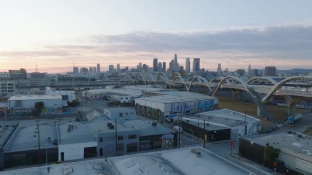 前進は夕暮れ時に工業地帯の上を飛ぶ コンクリートアーチとダウンタウンのスカイラインとモダンなデザインの道路橋 米国カリフォルニア州ロサンゼルス — ストック動画