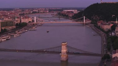 Tuna Nehri 'nin üzerinde ve kentte akan birçok köprünün üzerinde ileriye doğru uçar. Akşam karanlığında hava görüntüleri. Budapeşte, Macaristan.