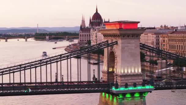 その後 広い川に広がるチェーン ブリッジの照らされた柱の上を飛ぶ ハンガリーの国会の美しい歴史的建造物 ブダペスト ハンガリー — ストック動画