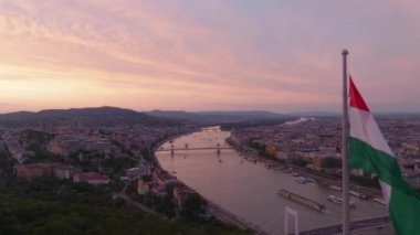 Nehrin yukarısındaki tepede Macar bayrağı dalgalanır. Renkli günbatımı gökyüzü ile romantik şehir manzarası. Budapeşte, Macaristan.