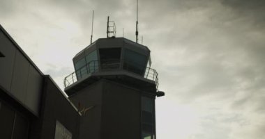 Havalimanı kulesinin alçak açılı görüntüsü gökyüzündeki bulutlara karşı. Hava trafik kontrolü, modern binanın silueti. Havaalanı ve havacılık kavramı.