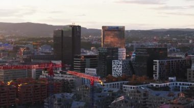 Günbatımında kentsel çevredeki bir grup modern yüksek binalar. İnşaat alanında kule vinçleri. Metropolis 'te altın saat. Oslo, Norveç.