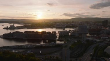Güneşin batışına karşı şehrin havadan romantik manzarası. Körfezdeki su yüzeyi renkli günbatımı gökyüzünü yansıtıyor. Oslo, Norveç.