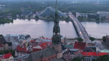 St. Peters Kilisesi 'nin yüksek ve ince kulesinin, geniş nehir ve karşı kıyıdaki modern binaların hava kaydırak ve pan görüntüsü. Riga, Letonya.
