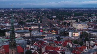 Alacakaranlıkta büyük şehrin hava görüntüsü. Eski şehirle tren istasyonu arasındaki modern alışveriş merkezi binası. İnşaat alanında kule vinçleri. Riga, Letonya.