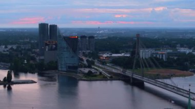Şehirdeki modern şehir gelişiminin inanılmaz bir görüntüsü. Vansu köprüsü, Daugava nehri üzerinde ve bir grup ofis ve ikâmet kuleleri alacakaranlıkta. Riga, Letonya.