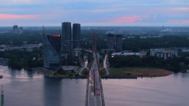 Modern kablolu TV 'nin hava kaydırak ve pan görüntüleri gece karanlığında şehir merkezindeki yol köprüsü ve yüksek katlı iş binalarında kaldı. Riga, Letonya.