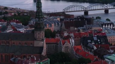 Gün batımından sonra St. Peters Kilisesi 'nin yüksek kulesinin hava kaydırağı ve pan görüntüsü. Nehir kıyısındaki eski kasabadaki tarihi binalar. Riga, Letonya.