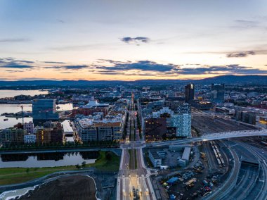 Central Tren İstasyonu 'ndaki modern şehir merkezinin renkli günbatımına karşı hava manzarası. Sakin su yüzeyi gökyüzünü yansıtıyor. Oslo, Norveç.